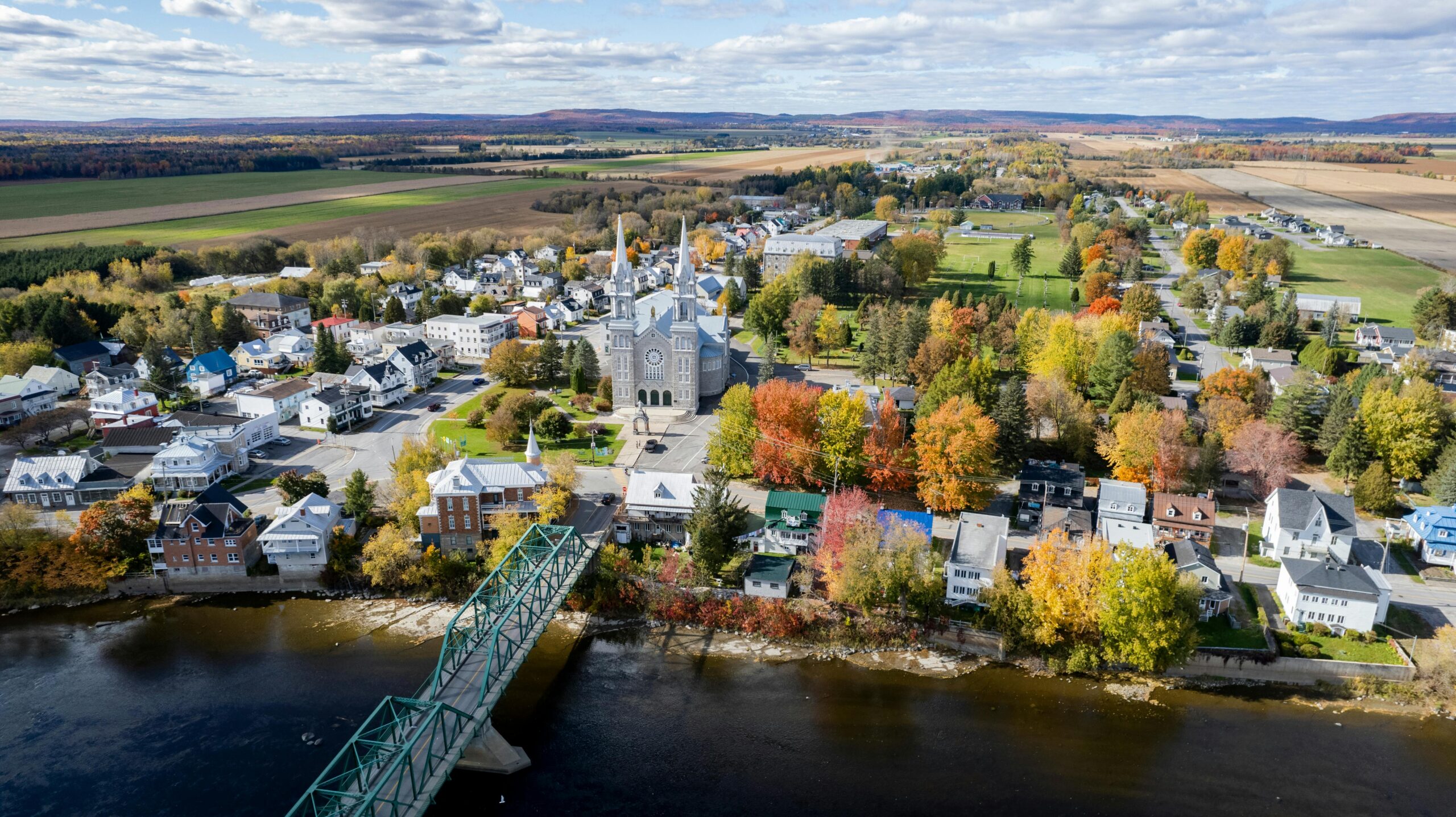 Une ville au Québec est prise en photo à partir du point de vu d'un drône. Les arbres sont dans les teines de l'automne et une église est posé au plein milieu.