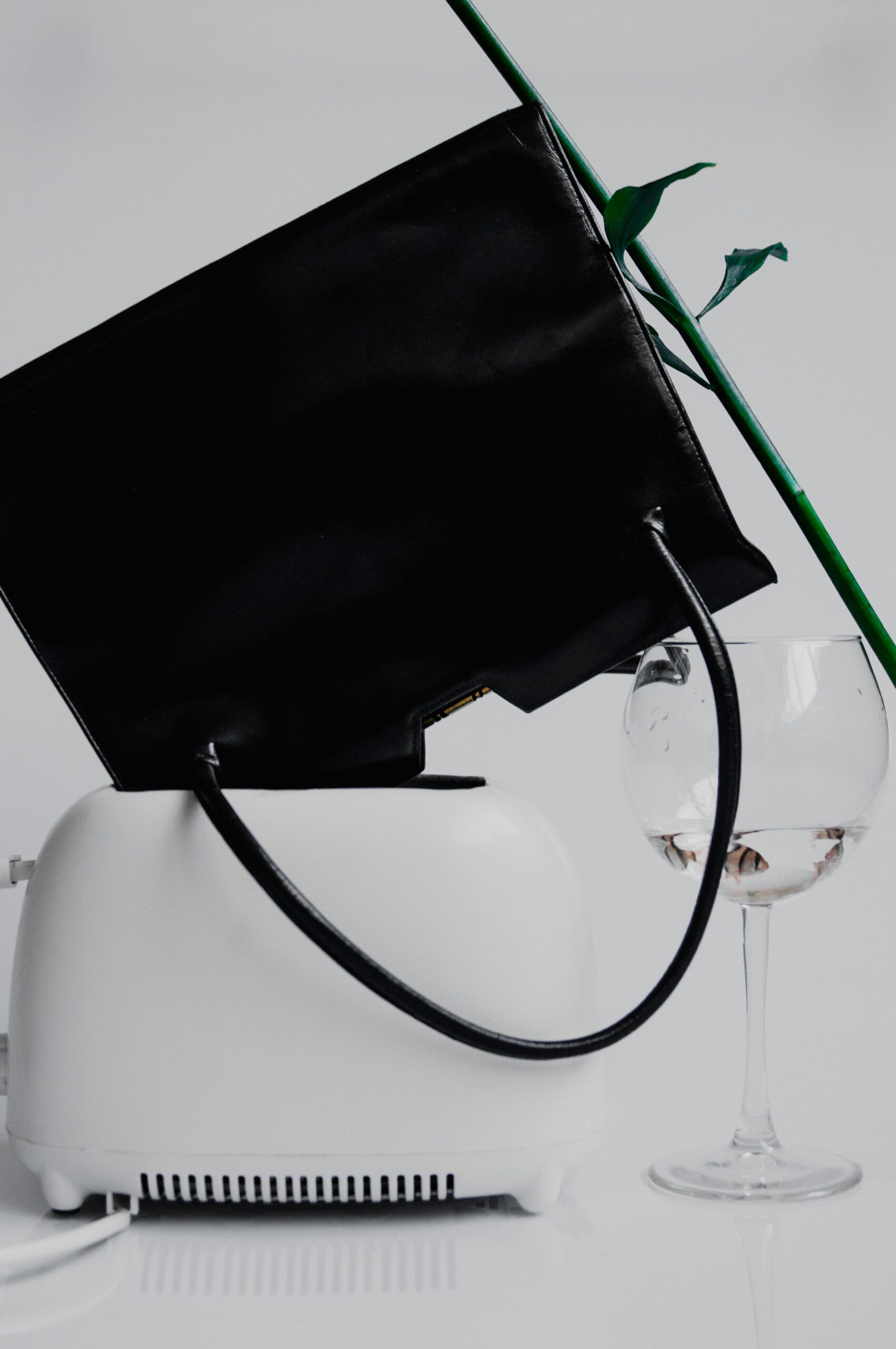 Un sac à main noir est renversé dans un grille-pain blanc et à côté d'un verre de vin rempli d'eau.