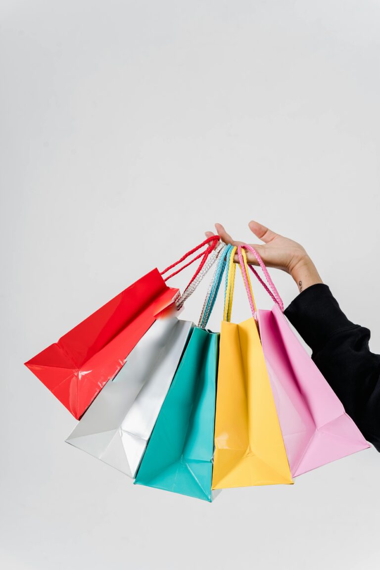 Une personne tient à bout de bras 5 sacs d'achat de couleurs différentes.